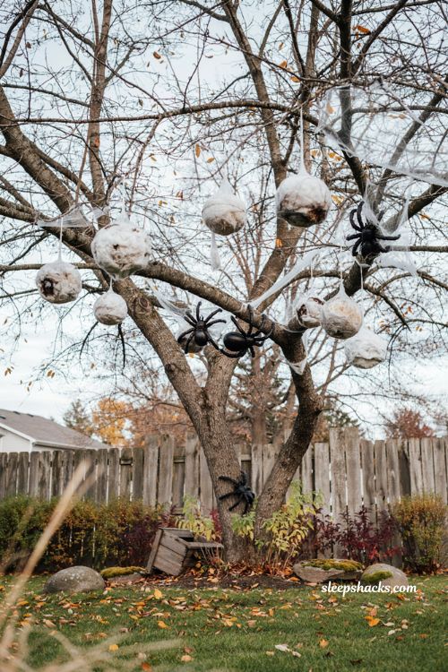 Creepy Halloween decorations with handmade spider egg sacs and oversized spiders in trees 