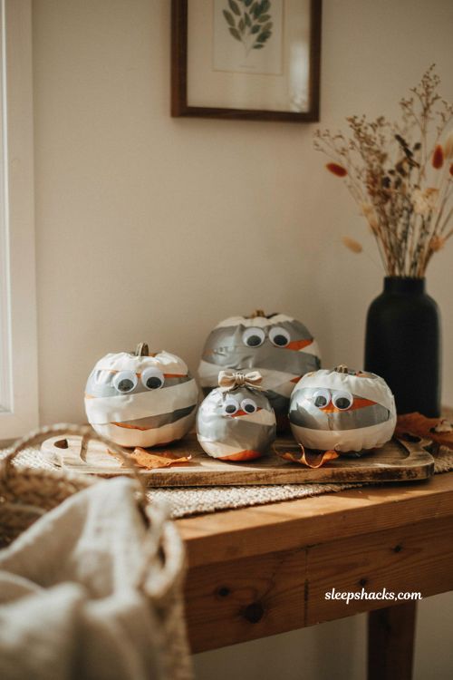 Easy Halloween mummy pumpkins wrapped in duct tape with googly eyes on a cozy autumn table