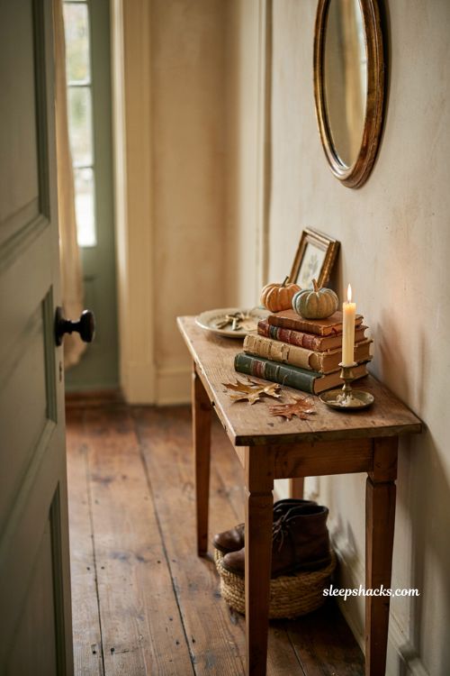Fall entryway table decor with mini pumpkins on stacked books and candle