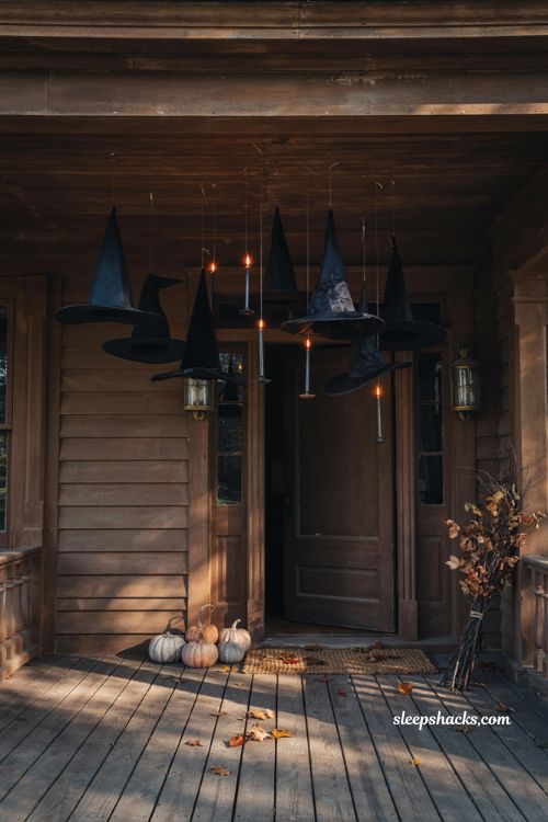 Floating black witch hats and taper candles suspended at different heights beneath a cozy Halloween front porch ceiling, magical dusk lighting, warm candlelight casting soft shadows, rustic cottage architecture, pumpkins and dried autumn branches, atmospheric DIY Halloween decor, charming spooky entrance, photorealistic editorial photography