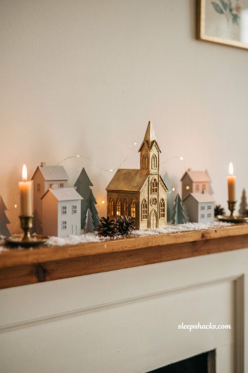 Gold foil accent Christmas village paper houses with a glowing centerpiece church on a cozy mantel 