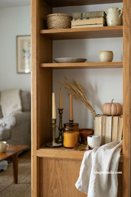 Grouped fall candles on open shelves with books and ceramic pumpkin