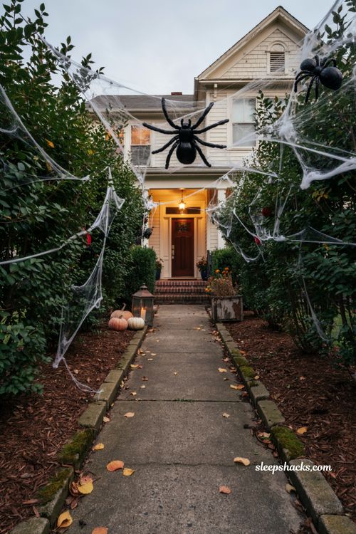 Halloween exterior decorations with cobweb covered bushes, oversized spiders, and autumn landscaping 