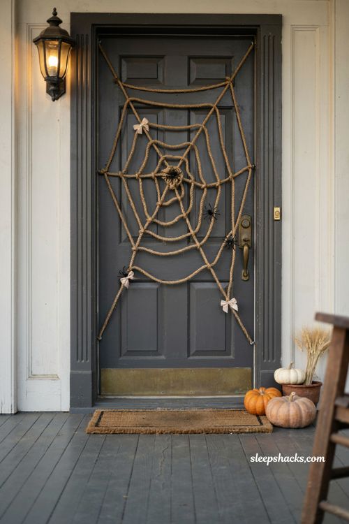 Halloween front door transformed into a large handmade spider web using textured rope, radiating web pattern stretched across dark wood door, small plastic spiders along the strands, tiny fabric bows, subtle pumpkins and warm porch details, creative DIY Halloween decor, striking spooky entrance, cozy autumn atmosphere, photorealistic editorial photography