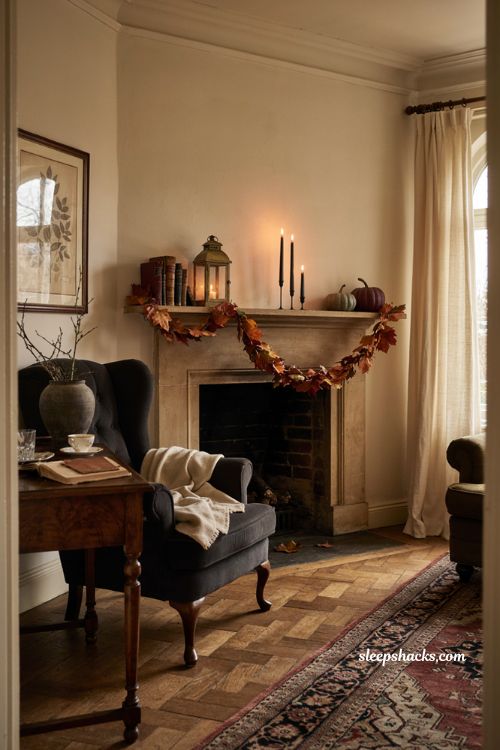 Halloween living room mantel with orange and rust garland, black candlesticks, lantern, pumpkins, and cozy autumn decor 