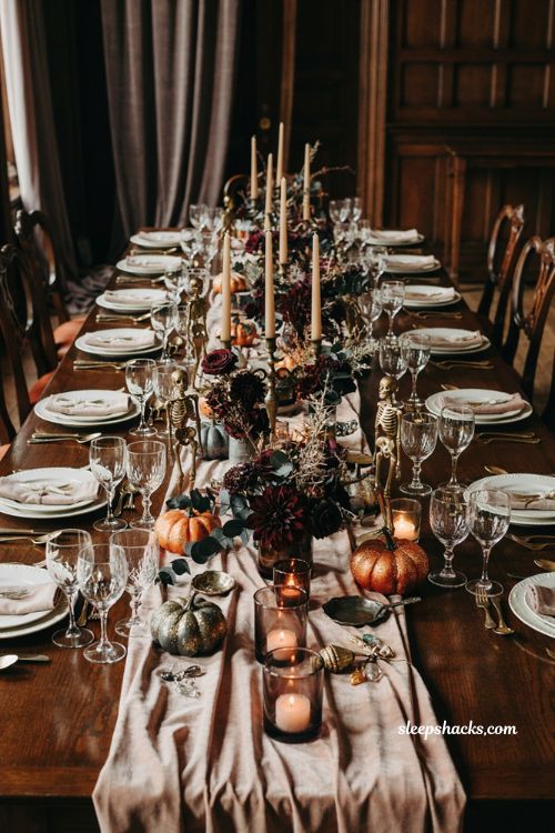 Pink glam Halloween dinner table with gilded skeletons dark florals and candles