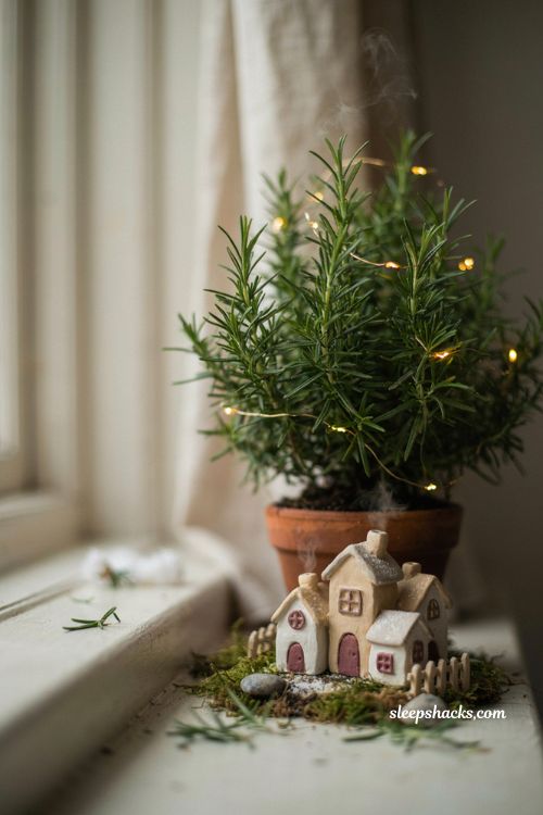 Tiny clay fairy Christmas village in a planter with miniature houses beneath a small evergreen tree 