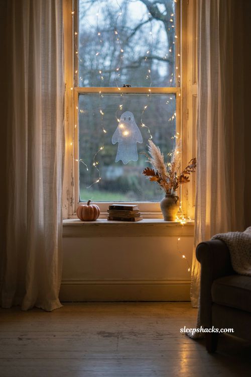 Twinkling fairy light Halloween window with sheer curtains and subtle ghost decor
