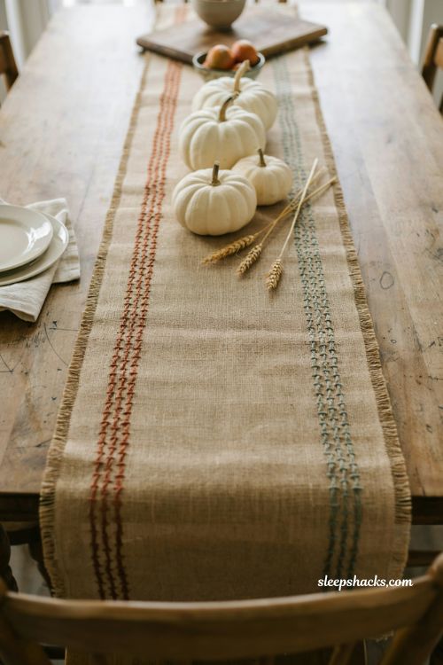 White pumpkin centerpiece on burlap runner with raffia stitching for a rustic fall table 