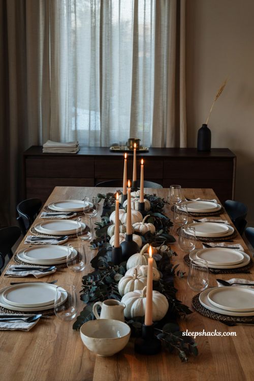 moody Thanksgiving table with dark foliage white pumpkins and matte black flatware