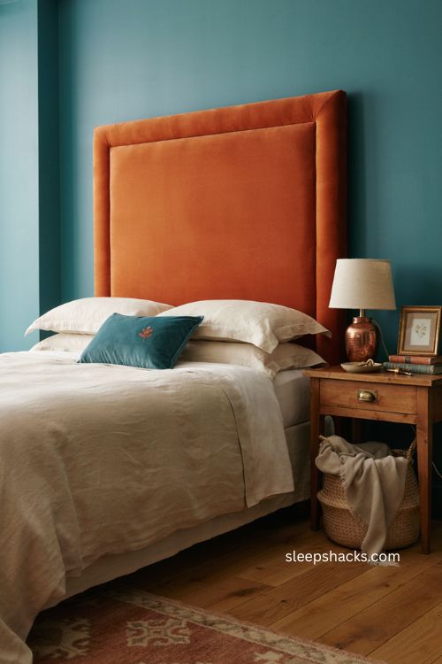 An upholstered orange headboard against teal walls in a cozy bedroom