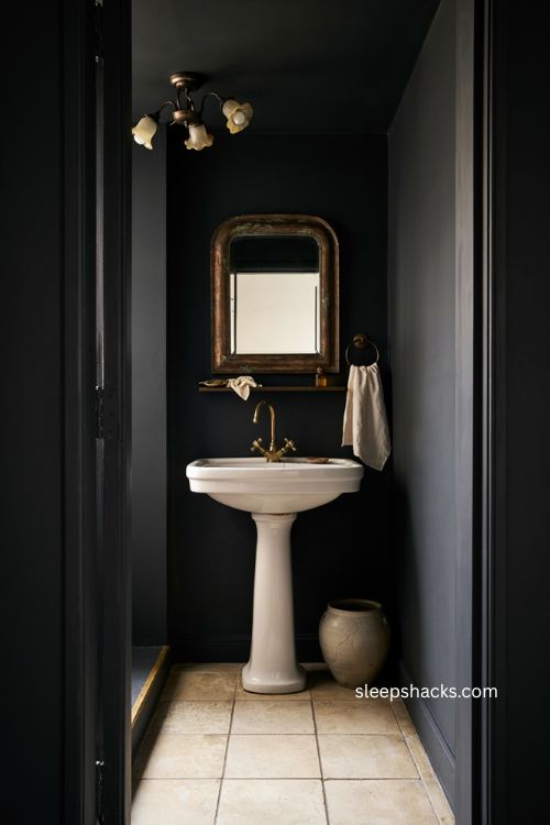 Black bathroom with warm bronze accents distressed mirror and pedestal sink