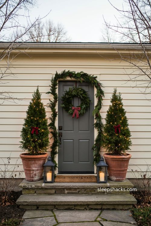 Cedar topiary trees in matching pots framing a farmhouse front door with Christmas lights 