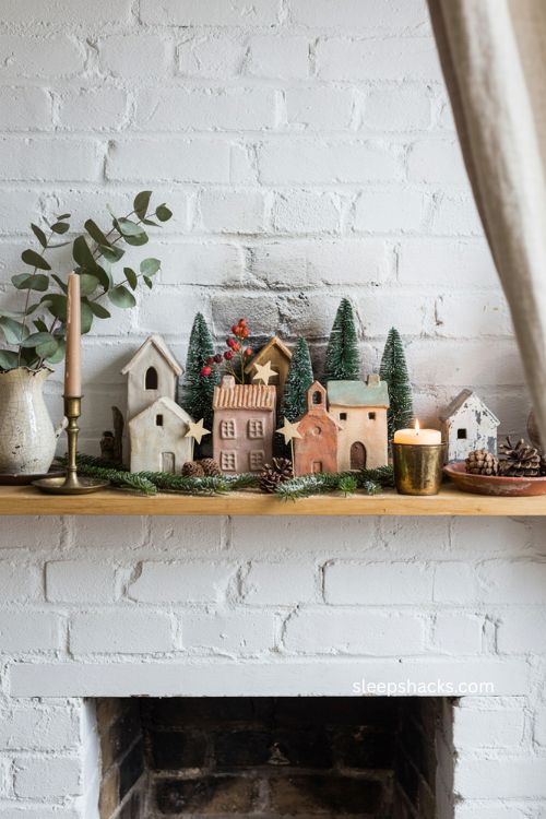 Christmas ceramic houses with miniature trees and greenery on a cozy fireplace mantel