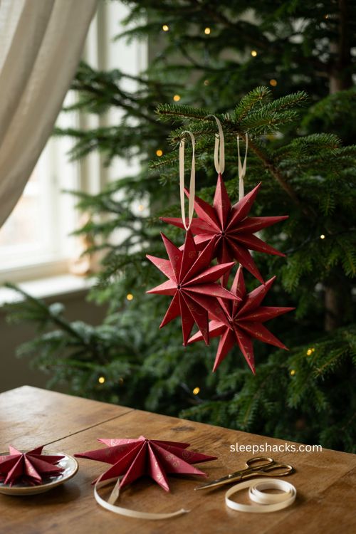Folded star ornaments with deep red woven paper strips and gold patterns on a traditional christmas tree 
