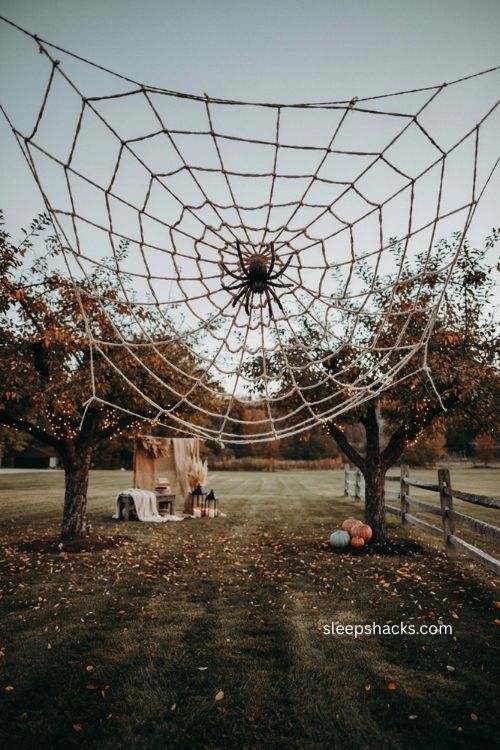 Giant backyard Halloween spiderweb with oversized spider trees and warm evening lights 