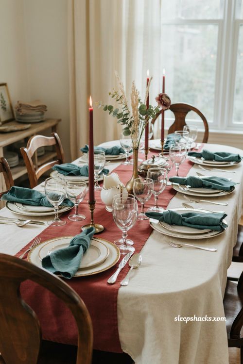 Gold rimmed Thanksgiving dinnerware with etched crystal glasses maroon candles and teal napkins
