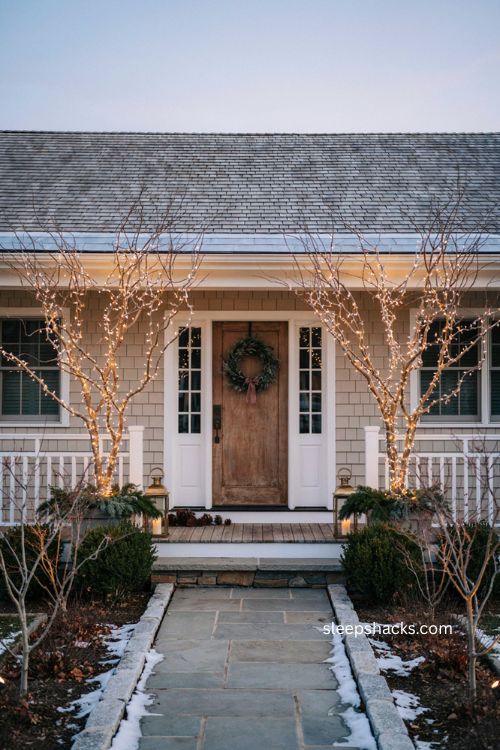 Lighted twig trees flanking front door with elegant Christmas porch decor and warm white lights 