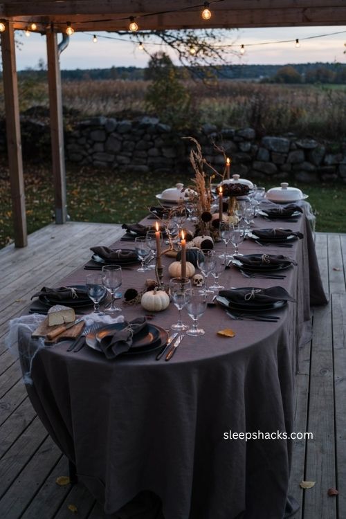 Moody backyard Halloween tablescape with black tableware candles pumpkins and dried florals 