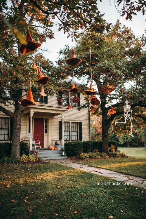 Orange witch hats hanging in trees with dangling skeleton and red front door Halloween yard decor