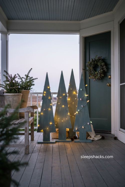 Painted evergreen wood christmas trees with warm lights beside a farmhouse front door 