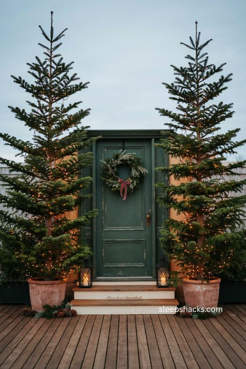 Slim Norfolk pine Christmas trees flanking front door in matching pots with warm lights 