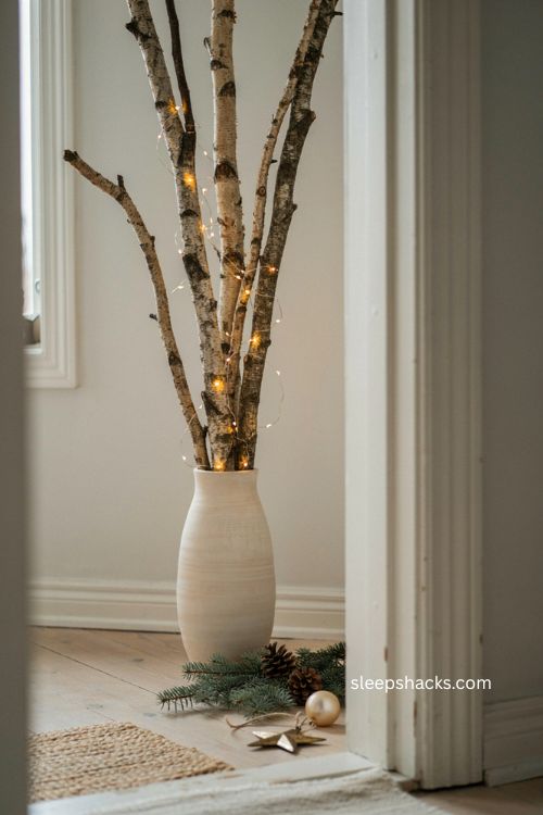 Small birch branch christmas decor beside apartment door with warm fairy lights and rustic vase 