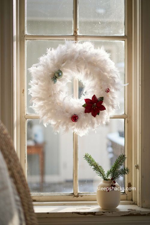White feather boa Christmas wreath with poinsettia and glowing window light 