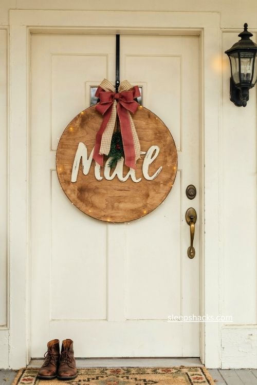 A diy round wood Christmas door sign with ribbon bow and fairy lights 