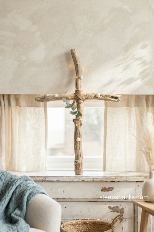 A medium-wide, straight-on editorial interior photograph of a handmade wooden Christmas cross tree finished in rich matte black chalkboard paint, displayed on a small rustic wooden easel beside a well-loved bookshelf in a peaceful farmhouse hallway. The cross has clean but slightly imperfect handcrafted edges, a velvety chalkboard surface, and a simple traditional silhouette that feels meaningful rather than decorative for decoration's sake. Inspired by vintage farmhouse Christmas styling, traditional Advent displays, and understated Christian home decor, the scene combines humble craftsmanship with a quiet sense of reflection and hope. A restrained palette of charcoal black, warm ivory, natural oak, muted evergreen, soft taupe, and subtle antique gold creates beautiful contrast without making the hallway feel dark or severe. Include a few understated evergreen sprigs, small cream-colored ornaments, a simple natural linen ribbon, and a tiny brass candle holder arranged nearby, allowing the black cross to remain the dominant focal point. Across the central beam, show a short, tasteful line of white chalk-marker lettering with the word peace, rendered as a small, natural part of the physical decoration rather than a digital text overlay. Preserve the matte, slightly powdery chalkboard finish, fine wood grain along the edges, realistic chalk-marker strokes, worn bookshelf surfaces, and the varied textures of old book spines without displaying additional readable text. A softly folded cream throw and a small woven basket near the bookshelf add the comfortable feeling of an everyday home. Gentle winter daylight enters from an adjacent window, revealing the subtle chalkboard texture and warm wooden details, while a nearby table lamp casts a quiet golden glow across the hallway and surrounding greenery. The overall mood feels contemplative, peaceful, personal, and quietly reverent, like a handmade Advent decoration that offers a small moment of reflection each time someone passes through the home. Soft colors that change the mood instantly, old textures that add warmth and depth, simple details that create lasting charm. no people, no text overlays, no watermarks, no blur, no bokeh, all surfaces in sharp focus, photorealistic, 4K resolution, editorial interior photography, Pinterest-worthy