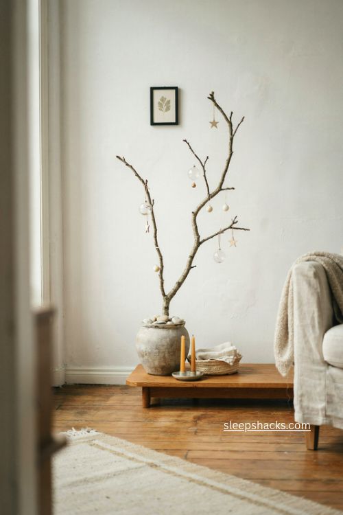 Bare branch christmas tree with delicate ornaments in a stoneware vase beside a bright window 
