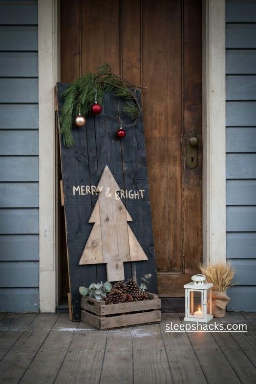 Black pallet Christmas sign with a rustic wooden tree and pinecone crate beside the front door