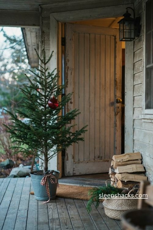 Charlie brown christmas tree in a galvanized bucket with a red bulb on a cozy farmhouse front porch