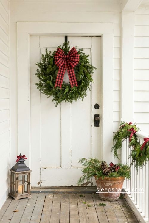 Christmas front door decor with a plaid ribbon wreath matching garland and cozy farmhouse accents