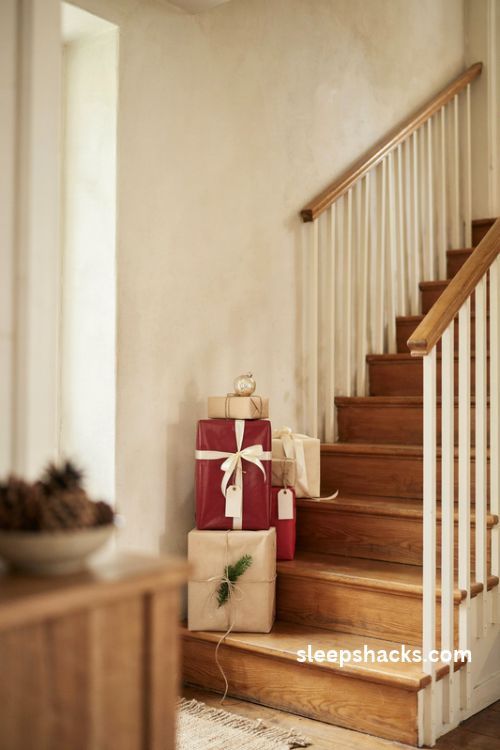 Christmas gift box stack on farmhouse stairs with red and kraft wrapping paper ivory ribbon rustic twine and evergreen sprigs
