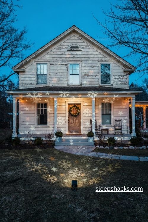 Christmas light projector displaying glowing snowflakes and stars across a cozy farmhouse front yard