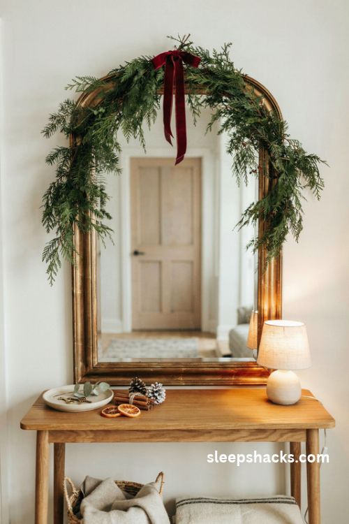 Christmas mirror decor with evergreen garland velvet ribbon bow and warm lamp light in a small entryway