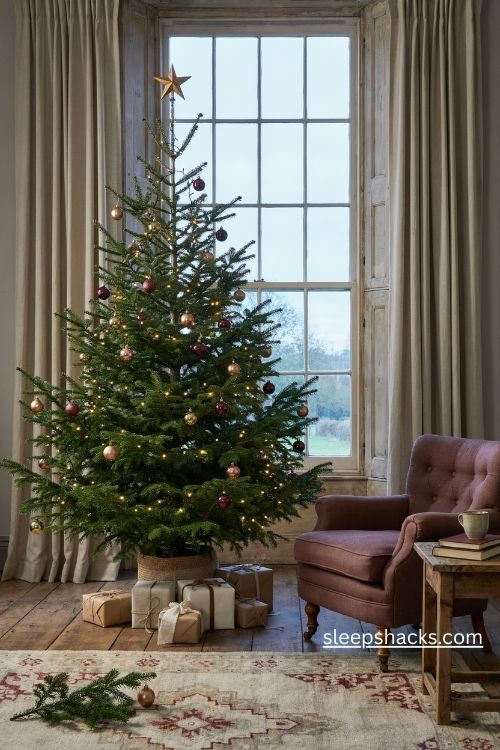 Christmas tree in front of a window with warm lights, neutral curtains, and cozy cottage decor