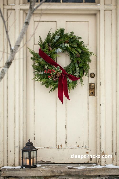 Christmas wreath sash with red velvet ribbon pinecones and berry picks on a rustic farmhouse door