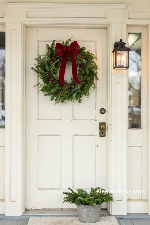 Classic evergreen Christmas wreath with a deep red velvet bow on a white front door