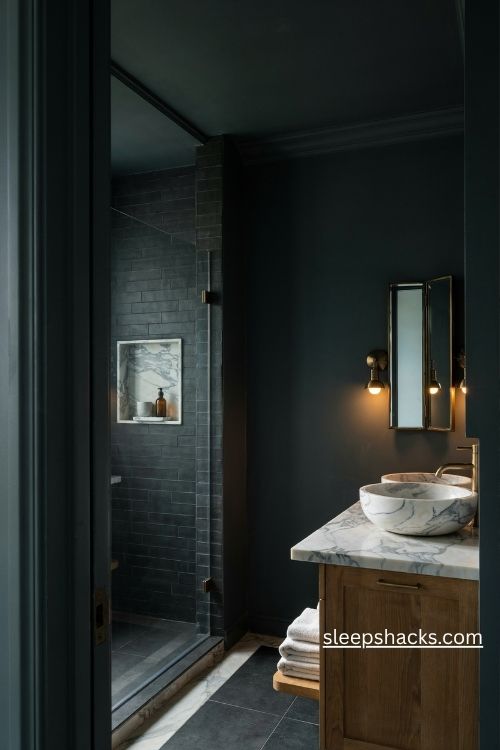 Dark bathroom with white veined marble countertop charcoal walls and warm brass fixtures