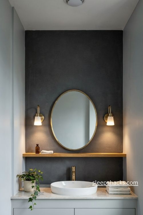 Deep charcoal accent wall bathroom with a round mirror and brass sconces 