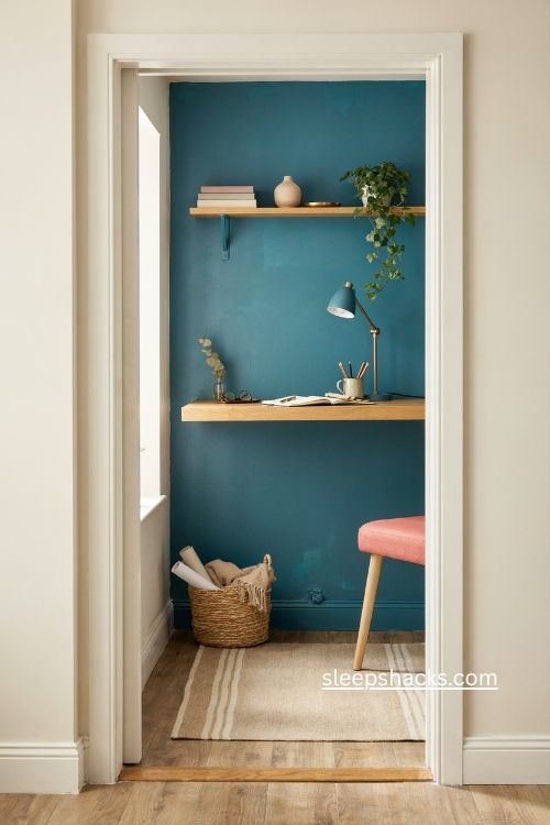 Deep teal closet home office with floating shelf slim lamp and warm wood desk
