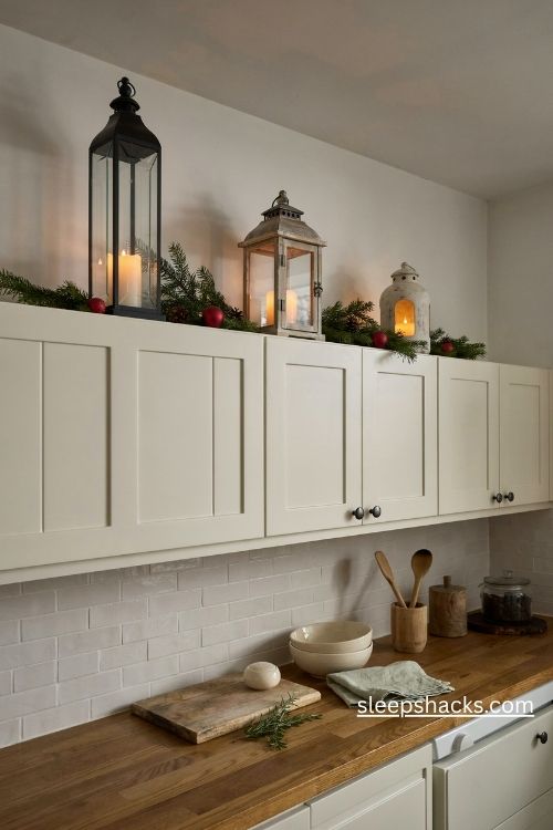 Farmhouse christmas lanterns with flameless candles and evergreen sprigs arranged above kitchen cabinets