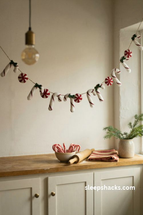 Felt candy cane Christmas garland with red and white striped decorations and tiny green bows on a cozy kitchen shelf