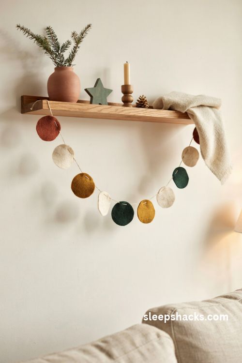 Felt circle Christmas garland in terracotta mustard green and cream hanging from a modern wooden shelf