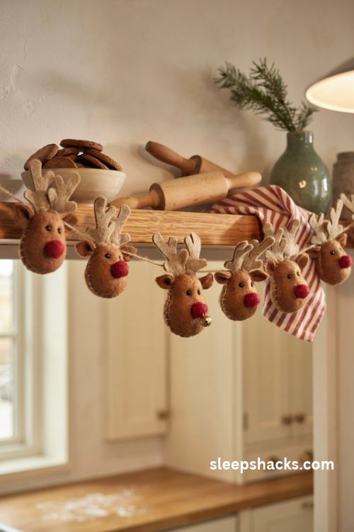 Felt reindeer Christmas garland with brown faces tan antlers and bright red noses on a cozy wooden shelf