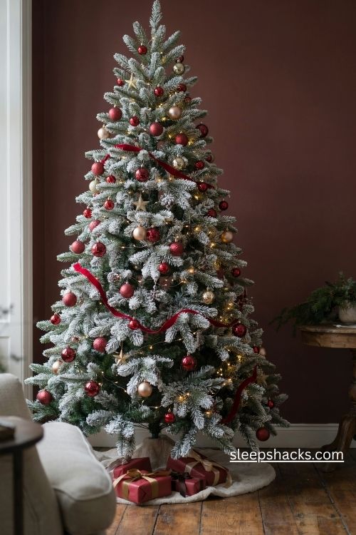 Flocked white christmas tree with red and gold ornaments against a dark wall