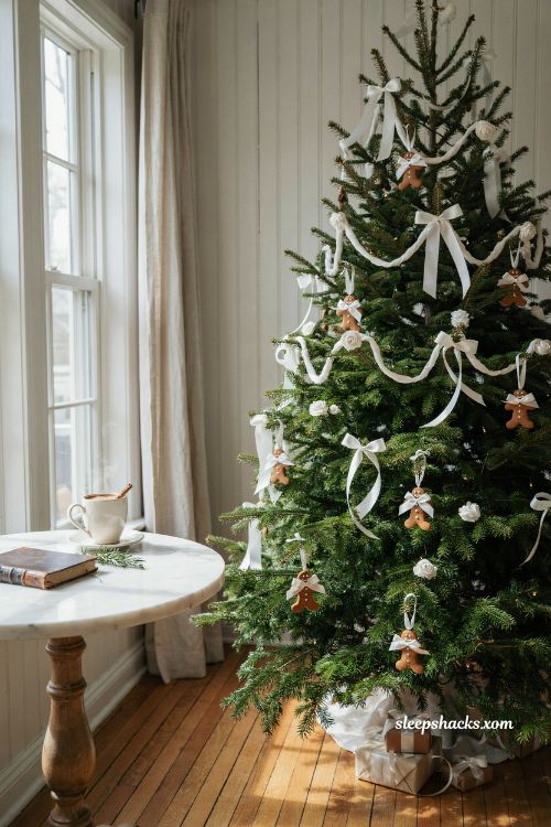 Gingerbread christmas tree decorated with white icing style satin ribbon bows in a sunlit living room