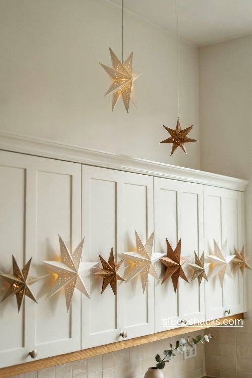 Glowing paper star lanterns in white kraft and soft gold above white kitchen cabinets